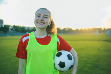 Portrait of a smiling teen girl football player with a soccer ball at sunset