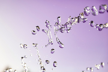 Water droplets frozen in the air with splashes and chain bubbles on a pink and purple isolated background in nature. Clear and transparent liquid symbolizing health and nature.