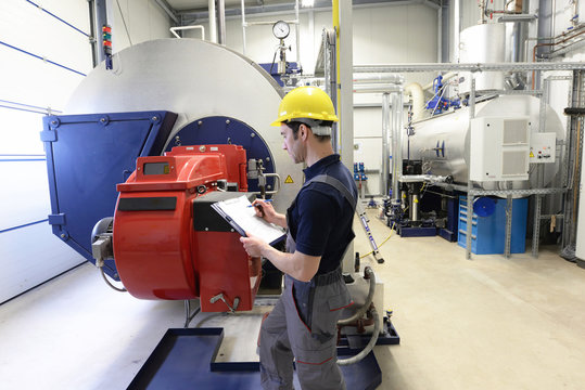 Industrial worker in a modern factory - interior closeup with machines - control of heating system boiler 