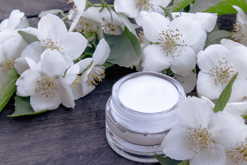 Fototapeta na wymiar Cosmetic cream in a glass jar with jasmine flowers on a wooden background.