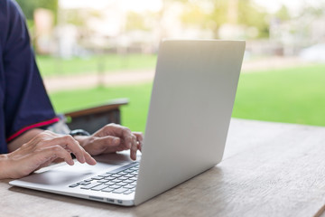 Woman hand using laptops and has a notebook and a pen with warm light