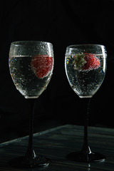 Close up. Wine Glasses filled with Sparkling Drink. Strawberries float in the sizzling liquid. Isolated on black background. Wooden table. Copy space.
