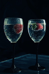 Close up, macro. Wine Glasses filled with Sparkling Drink. Strawberries float in the sizzling liquid. Isolated on black background. Copy space.
