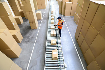 Arbeiter im Versandlager eines Onlinehandels mit Barcodescanner am Fliessband mit Paketen  //...