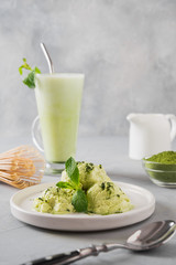 Green matcha ice cream and tea in latte glass on grey table.