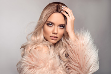 Sexy woman wears in pink fur coat. Ombre blond hairstyle. Beauty fashion blonde portrait. Beautiful girl model with makeup, long healthy hair style posing isolated on studio grey background.