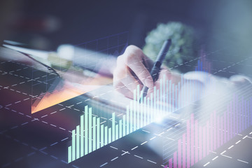 Financial forex graph displayed on hands taking notes background. Concept of research. Multi exposure