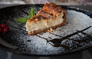 a slice of cottage cheese cheesecake on a large black plate decorated with mint and cranberries