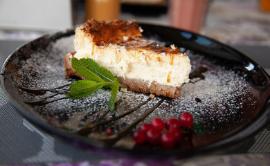 a slice of cottage cheese cheesecake on a large black plate decorated with mint and cranberries