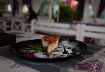 a slice of cottage cheese cheesecake on a large black plate decorated with mint and cranberries