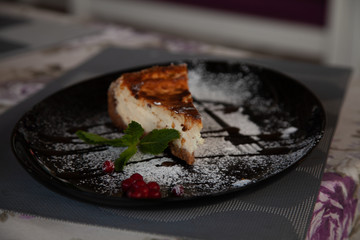 a slice of cottage cheese cheesecake on a large black plate decorated with mint and cranberries