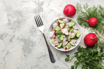 Fresh radish and cucumber salad and greens on a light concrete table. Salad of spring vegetables. ingredients for making salad. top view