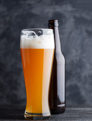 Wheat unfiltered beer in a glass of bright saturated color and a beer bottle on a dark background