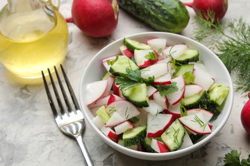 Fresh radish and cucumber salad and greens on a light concrete table. Salad of spring vegetables. ingredients for making salad.