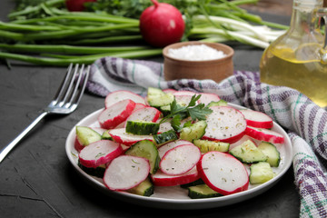 Fresh radish and cucumber salad and greens on a black concrete table. Salad of spring vegetables. ingredients for making salad.