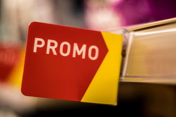 A red and yellow promo sign on a supermarket shelf.