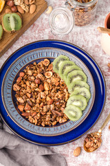 honey granola with nuts, in two blue plate, kiwi slices, for breakfast, glass jar, on table, vertical, view