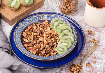honey granola with nuts, in two blue plate, kiwi slices, breakfast, glass jar, on table, horizontal