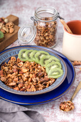 honey granola with nuts, in two blue plate, kiwi slices, breakfast, glass jar, on table, vertical