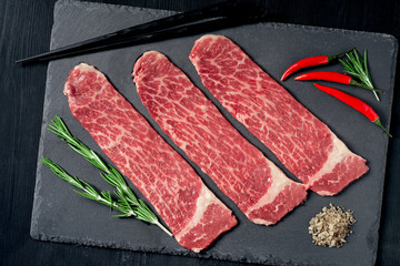 Pieces of raw marble beef black Angus for grilling on a stone Board on a dark background
