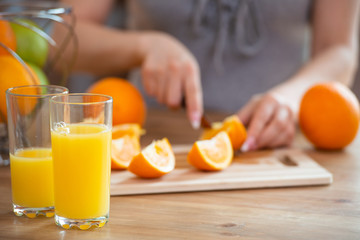 cooking, food and concept of veganism, vigor and healthy eating - close up of female hand cutting orange on slices