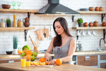 sporty young woman is cutting fresh orange for fruit juice in the kitchen. Horizontal indoors shot