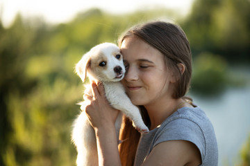 A girl holding a labrador puppy and smiling. At sunset in the forest in summer. The concept of friendship, happiness, joy and childhood