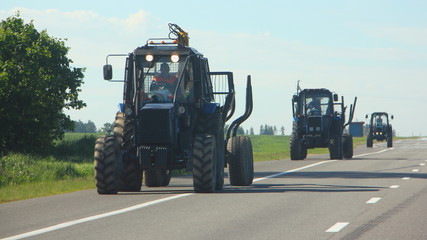 Three empty wheeled tractor timber carriers go on the side of the asphalt road on a summer day for loading, front view © Ilya