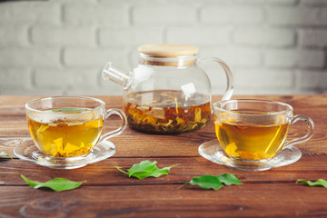 glass teapot with cup of black tea on wooden table