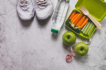 Lunch box with vegetables next to sneakers, water bottle and apples