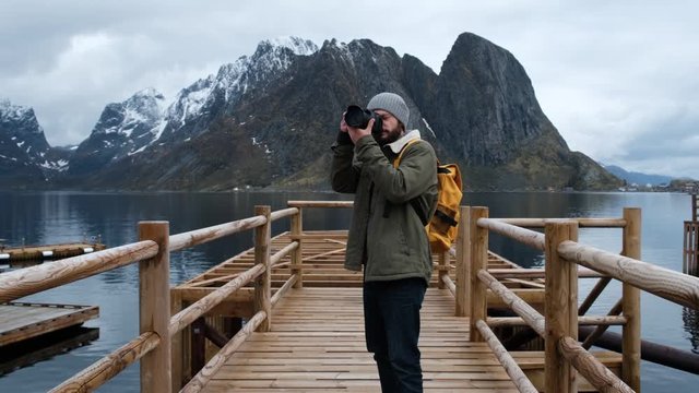 Professional photographer male taking photograph of valley with DSLR wearing backpack photographing scenic landscape nature travel adventure Norway.