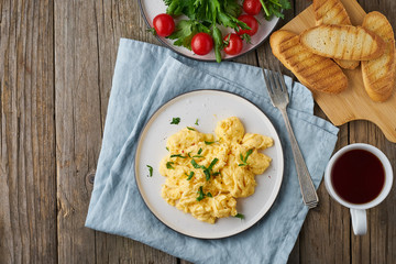 Scrambled eggs, omelette, top view, copy space. Breakfast with pan-fried eggs, cup of tea, tomatoes on old wooden table