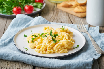 Scrambled eggs, omelette, side view. Breakfast with pan-fried eggs, cup of tea, tomatoes on old rustic wooden table