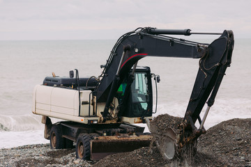 Heavy excavator working on the beach, excavator digs stones and pebbles