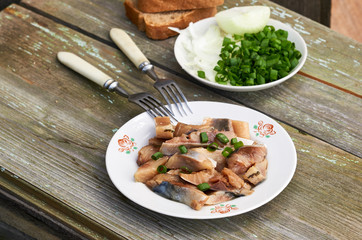 Slices of salted herring with green onions on a wooden table
