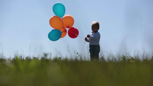 Little boy, toddler, child playing with colorful balloons in the park on kids day, sunny summer afternoon in nature