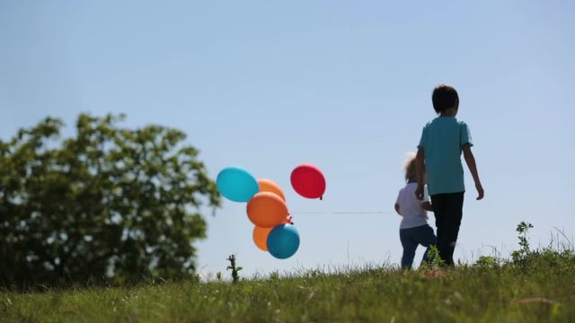 Little boys, toddler and his older brother, children playing with colorful balloons in the park on kids day, sunny summer afternoon in nature