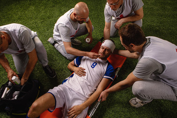 Soccer player received a head injury during the game. Sport Doctors provide first aid to player on a professional football field © Alex