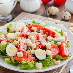 Caesar salad with salted salmon on a white plate, selective focus