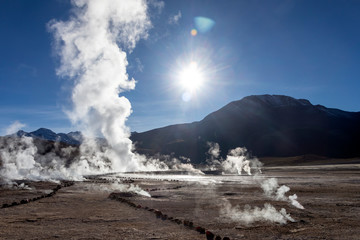 Bright rising sun above erupting Hot Geyser Of Steam in El Tatio Geysers field at early morning sunrise, Atacama desert, Chile