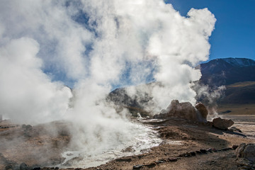 Atacama desert, Chile: Bright rising sun behind erupting Hot Geyser Of Steam in El Tatio Geysers field at early morning sunrise
