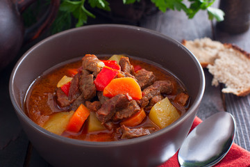 Pot of hungarian goulash on rustic wood background with chili peppers and laurel and copy space