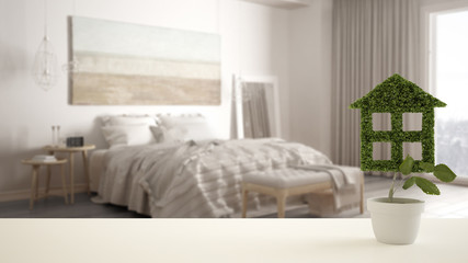 White table top or shelf with green plant in pot shaped like house, modern blurred bedroom in the background, interior design, real estate, eco architecture concept idea