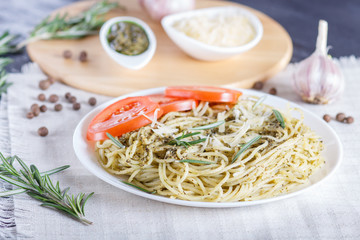 Spaghetti pasta with pesto sauce, tomatoes and cheese on a linen tablecloth.