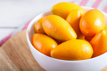 kumquats in a white plate on a white wooden background