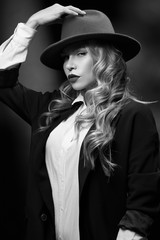 Portrait of gorgeous woman with makeup and long curls looking sexy at camera and posing in studio. Serious female wearing smart suit touching hat with hand. Concept of beauty and sensuality.
