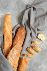 Still life with fresh French baguettes in a gray linen towel on a concrete background. Whole and sliced. Vertical orientation. Flat lay.