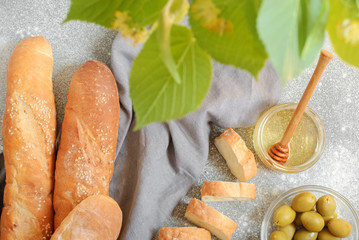 Still life with fresh French baguettes in a gray linen towel, honey and olives on a concrete background. Whole and sliced. Horizontal orientation. Flat lay.