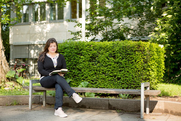 Fototapeta premium Lady Sitting on City Bench while Reading a Book