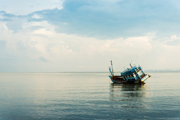 The abandoned ship floated on the shallow water side. The waves were calm in the morning. It's too old to fight the ocean waves. Has a background for copy space.